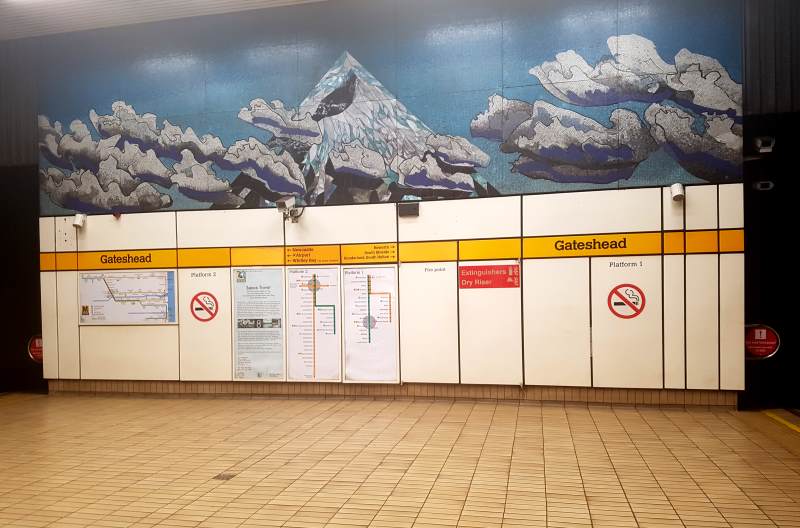 Een mozaïek van wolken met uitzicht op een berg is aangebracht boven de bewegwijzering van het metrostation van Gateshead.