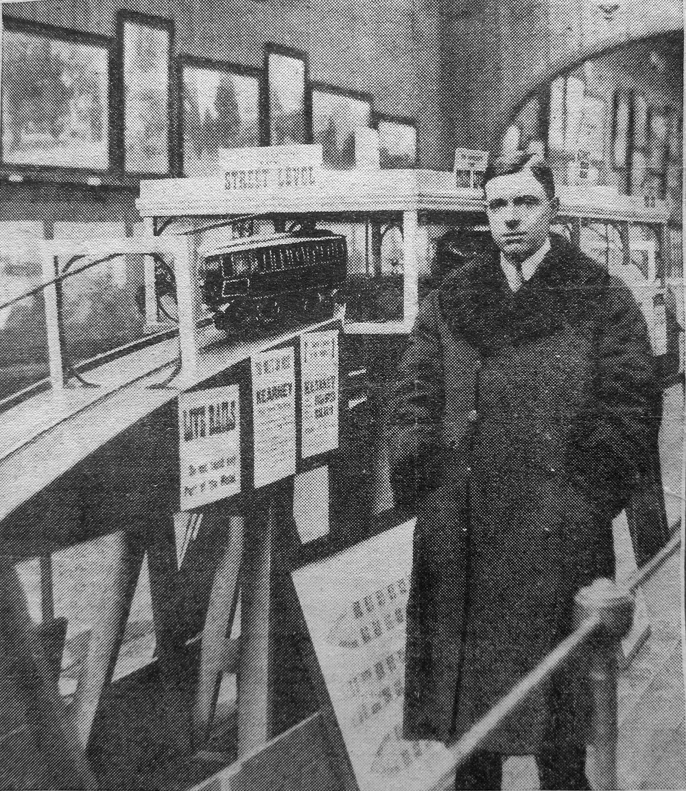 An Edwardian gentleman in a dark coat stands next to a scale model of a railway descending down a steep gradient