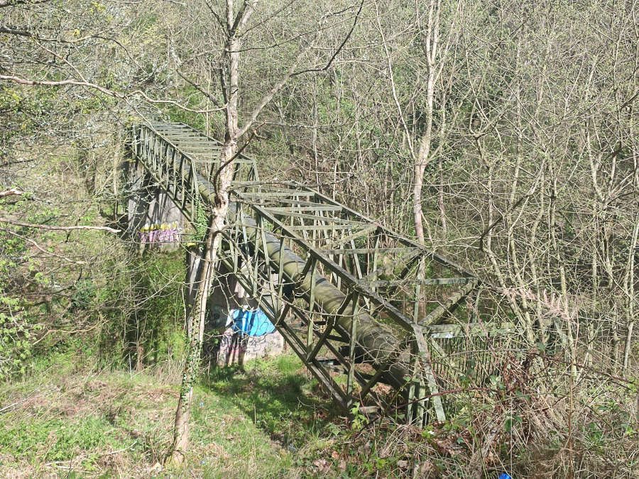 A graffiti-covered pipe crossing a ditch inside a steel frame