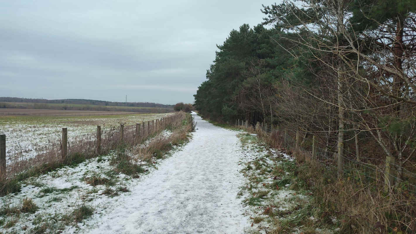 A dirt path by a farm lightly covered in snow