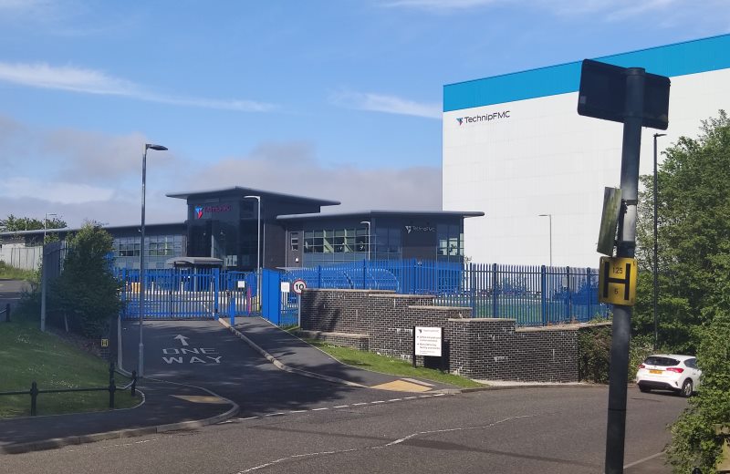 An *exceedingly* evil looking office building next to a gigantic white cube bearing the logo "TechnipFMC".