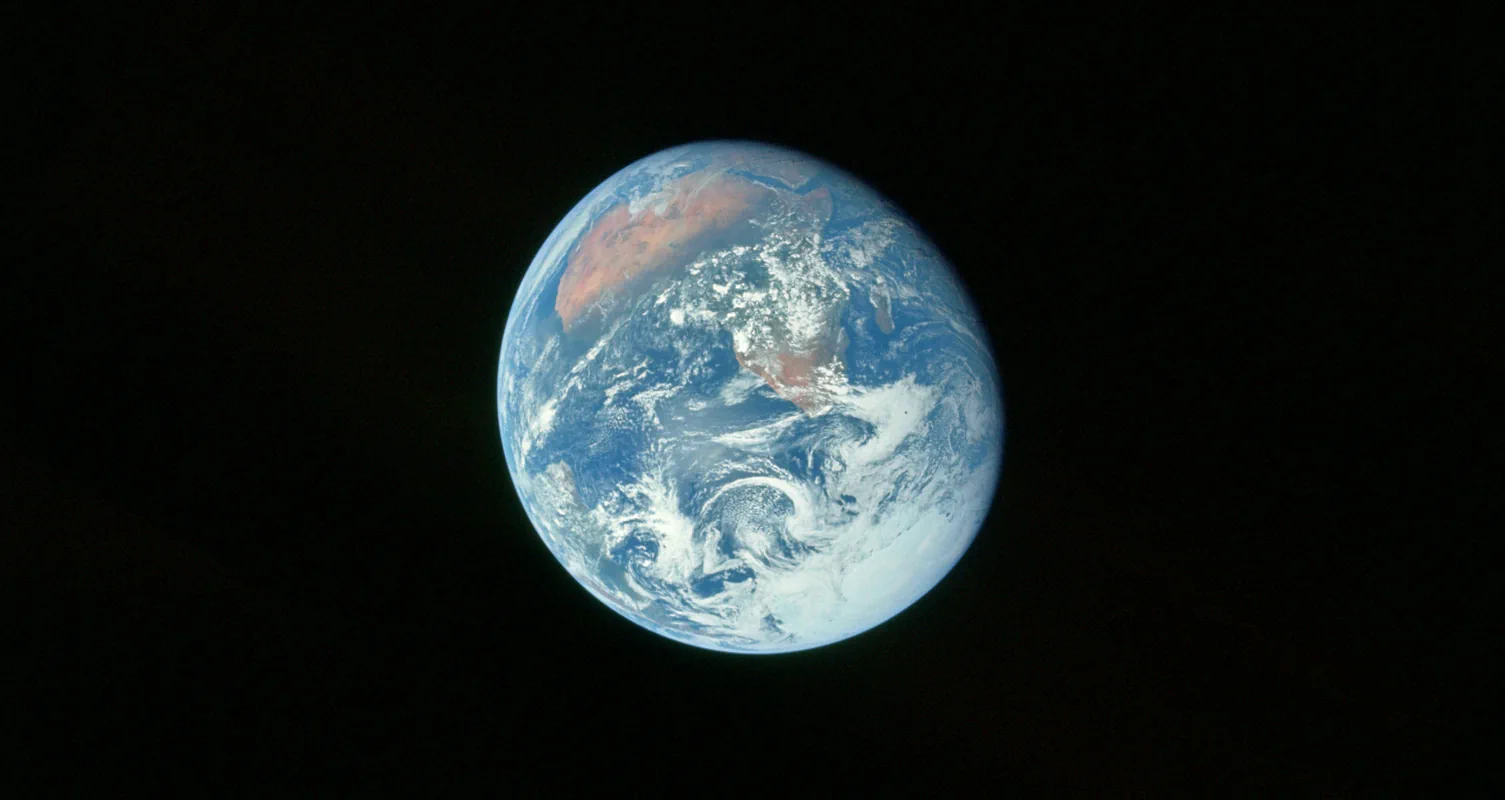 De Aarde, haar schijf blauw met water, de groene bossen en gouden woestijnen van Afrika die bijna onder een wit wolkendek uitkomen